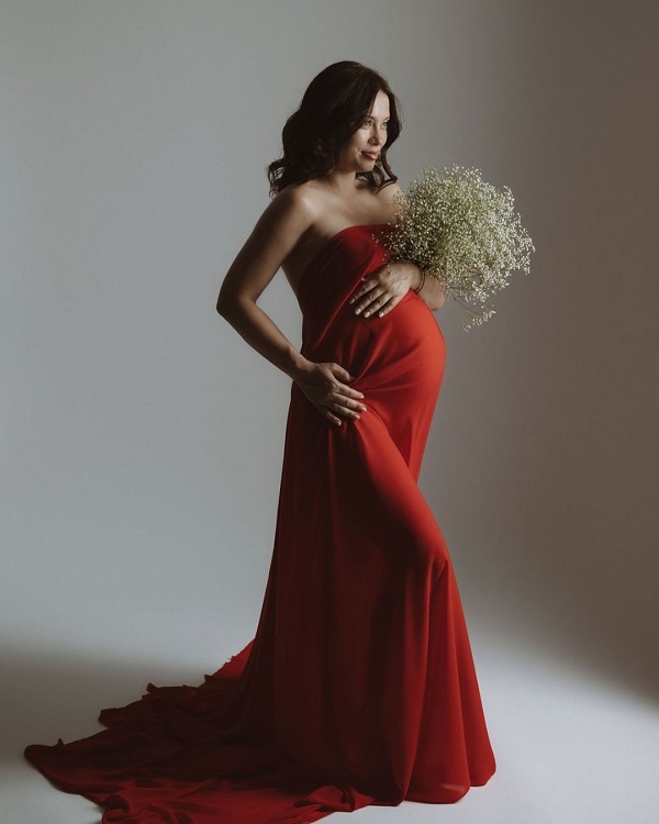 anca dumitra in rochie rosie cu buchet de flori albe in mana insarcinata