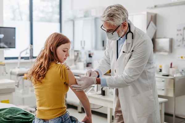 medic cu parul grizonat vaccineaza o adolescenta imbracata in galben