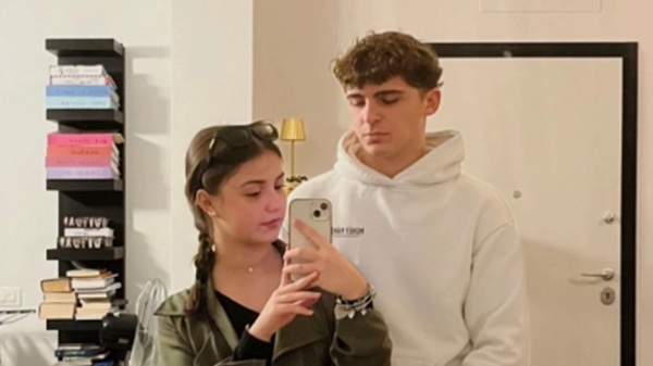 o fata cu parul prins in coada impletita alaturi de un baiat in hanorac alb fac un selfie