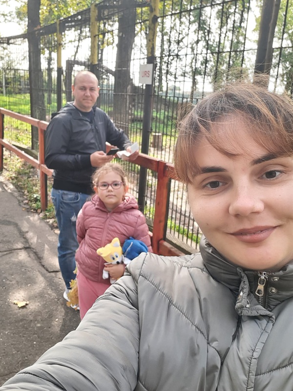 femeie imbracata in gri face un selfie cu sotul si fetita in spate