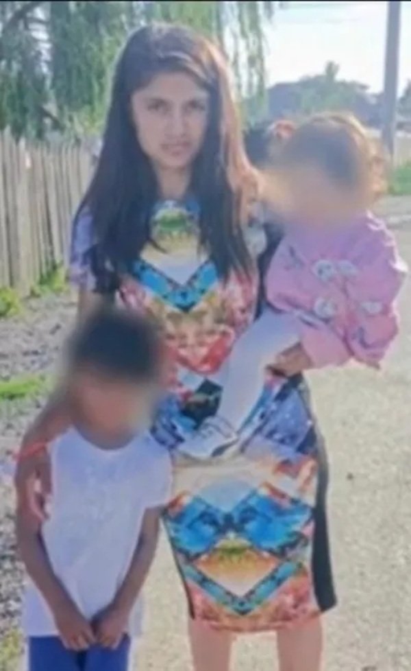 femeie satena cu par lung cu un copil in brate si unul de mana