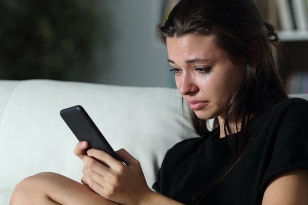 femeie care se uita la telefon si plange