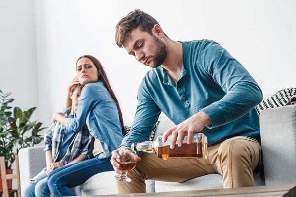 mama isi tine copilul in brate in timp ce tata isi toarna alcool in pahar