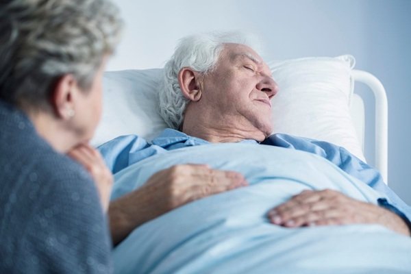 femeie cu parul grizonat langa un barbat in varsta pe patul de spital
