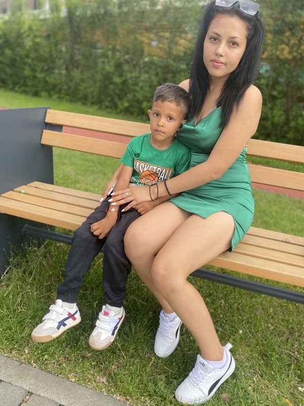 femeie in rochie scurta verde cu baiatul ei pe o banca