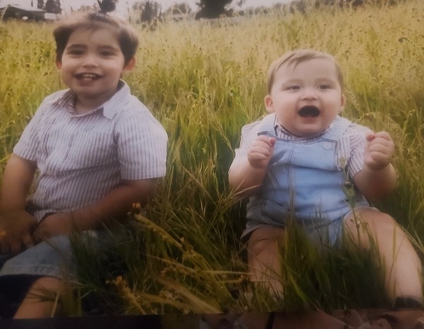 doi copii imbracati in tricou alb si pantaloni albastri stau pe iarba