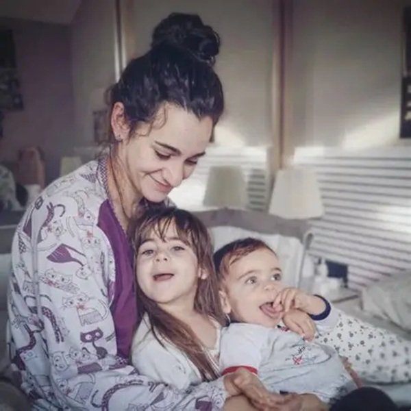o mama cu parul prins in coc cu cei doi copii ai ei in pat