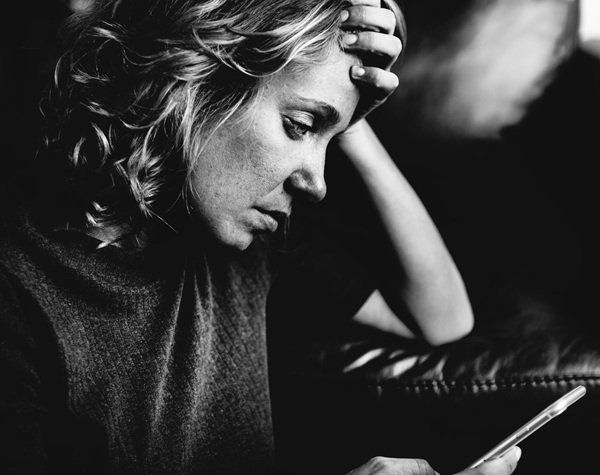 foto alb negru cu o femeie cu parul scurt care se uita la telefon trista