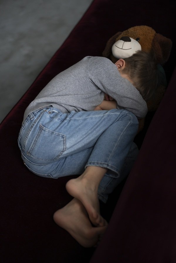 baiat imbracat in pijamale sta ghemuit pe o canapea