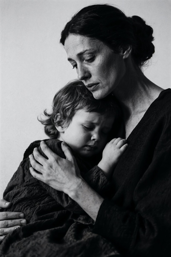 poza alb negru cu o mama cu parul prins in coc care isi tine copilul in brate