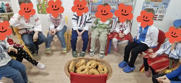 copii cu fetele acoperite in costume populare de jur imprejurul unui cos cu colaci