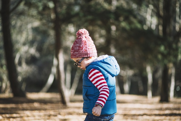copil cu vesta albastra si fes roz afara