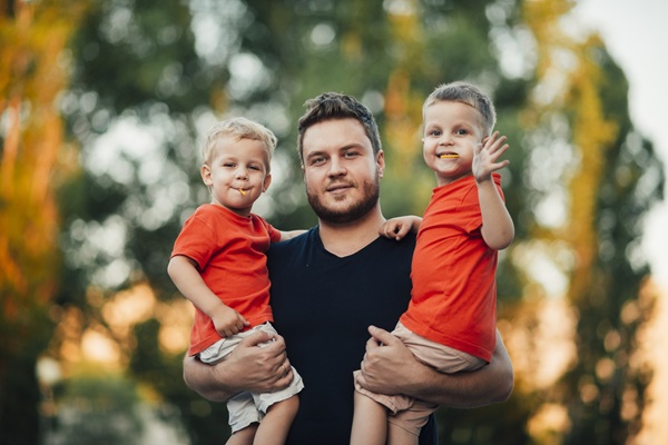 barbat cu tricou negru cu doi baieti gemeni in brat