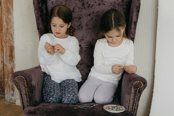 doua fetite se joaca cu bratarile pe un fotoliu