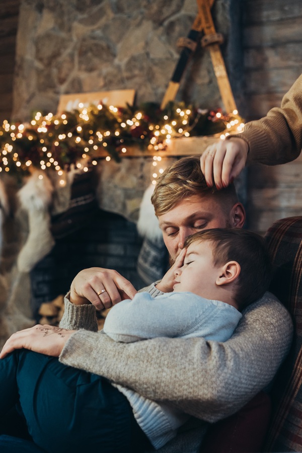 barbat isi tine copilul in brate langa bradul de craciun