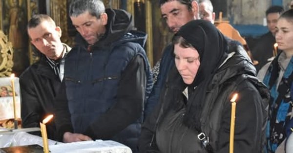 mai multi oameni in haine negre la o inmormantare cu lumanare aprinsa