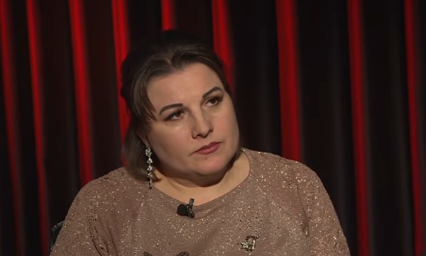 femeie cu parul rosu scurt cu ruj rosu si bluza aurie in spate o copertina grena