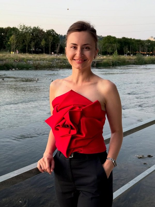 femeie imbracata in top rosu cu trandafir si pantaloni negri pe malul unei ape