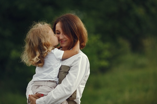 mama cu parul saten isi tine in brate copilul blond care o pupa pe obraz