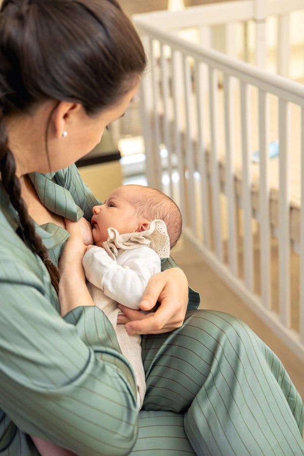 mama imbracata in pijama verde isi alapteaza copilul langa patutul de lemn