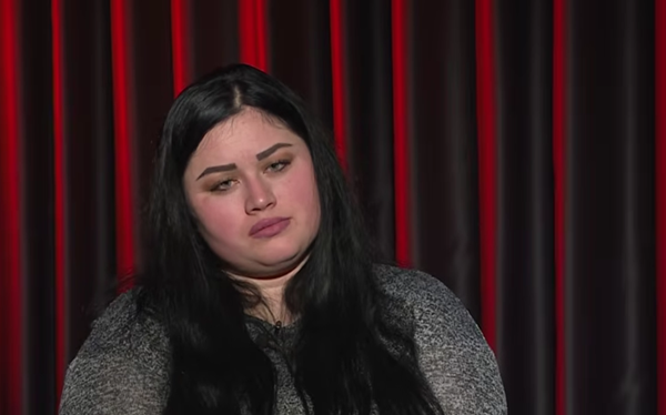 femeie bruneta cu parul lung in bluza gri pe fundalul unei cortine grena