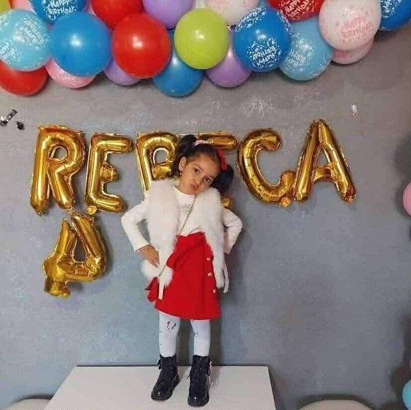 fetita cu bluza alba si dusta rosie langa niste baloane