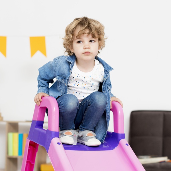 copil in geaca de blugi si tricou alb se da pe tobogan