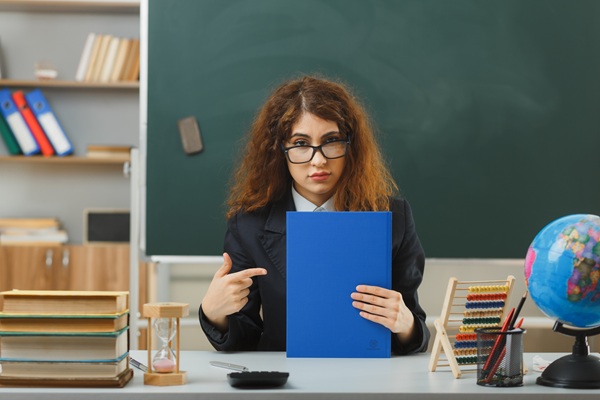 profesoara cu parul saten cret tine un catalog albastru in mana la catedra