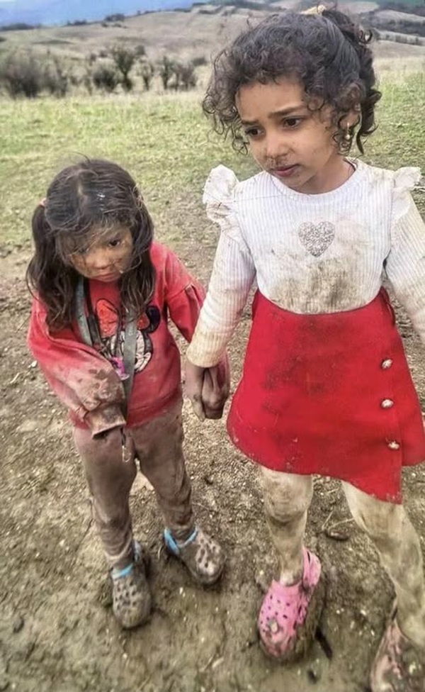 doua fetite pline de noroi imbracate in alb si rosu pe un deal
