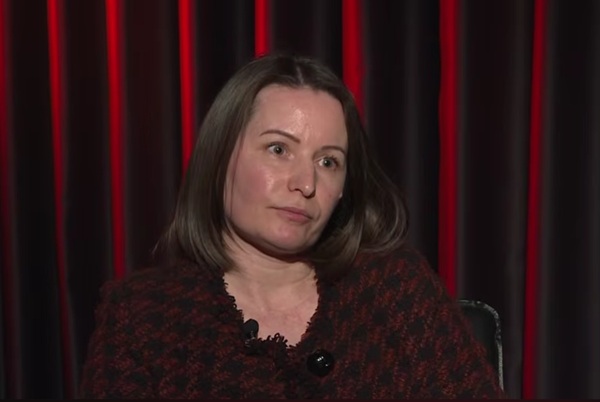 femeie satena cu parul mediu sta cu capul intr-o parte pe fundal copertina rosie