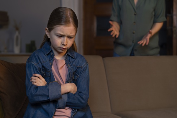 fata suparata sta cu mainile incrucisate in timp ce o adult o cearta din usa