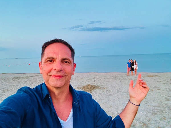 dan negru in camasa albastra pe plaja prezinta familia in spatele lui langa mare