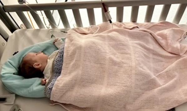 bebelus imbracat in albastru invelit in paturica roz in patut