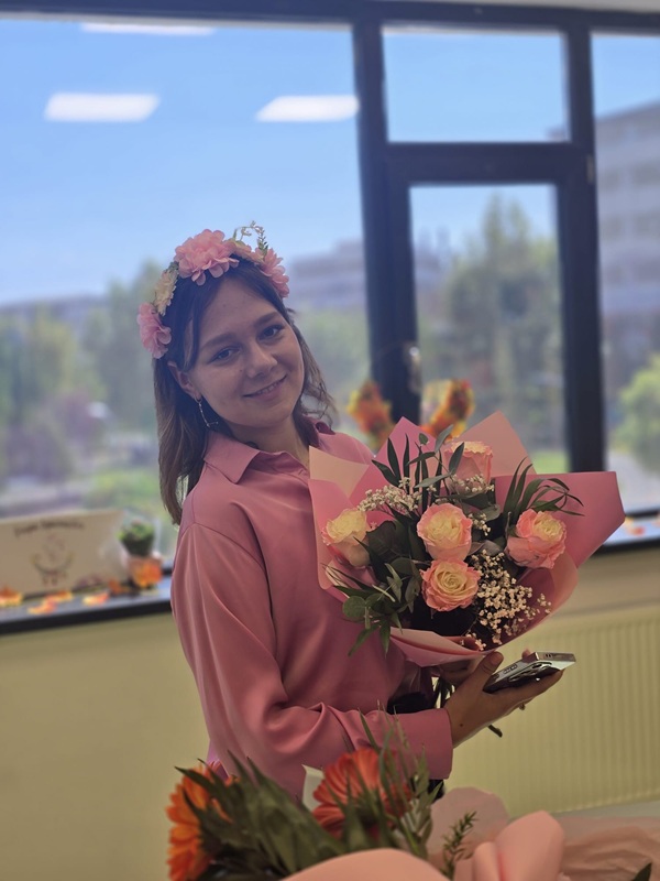 educatoare tanara imbracata in roz tine un buchet de flori in brate