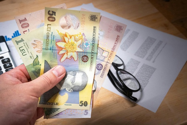 o mana tine mai multi bani romanesti lei pe o masa langa o perecge de ochelari de vedere si un calculator
