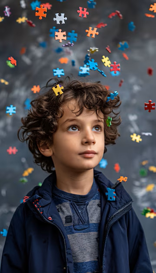 baiat imbracat in albastru cu parul cret inconjurat de piese de puzzle