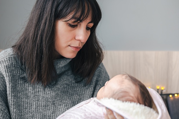mama bruneta imbracata in gri tine bebelusul in brate