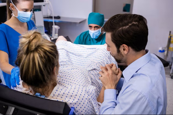 echipa de medici examineaza ginecologic o femeie in prezenta partenerului ei in sala