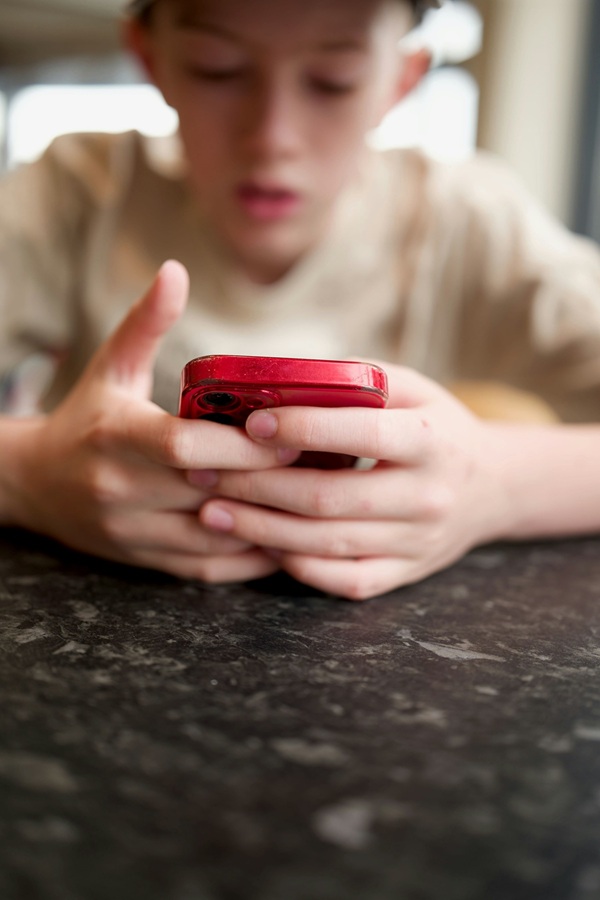 baiat blond se joaca pe un telefon rosu