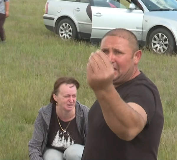 femeie care plange si barbat disperat care ridica mana in aer pe un camp