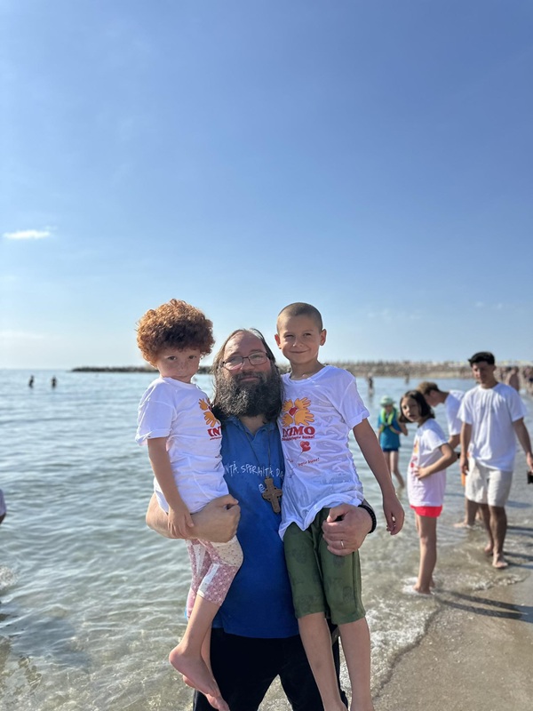 preotul dan damaschin in tricou albastri tine in brate doi copii la mare