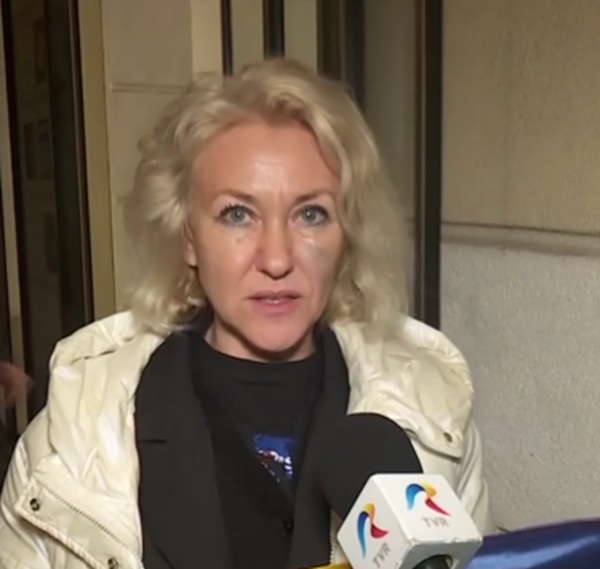 femeie blonda cu bluza neagra si geaca alba