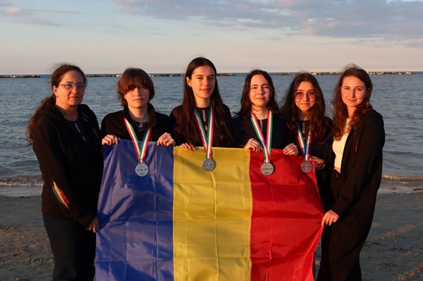 4 fete si 2 profesoare tin in mana steagul romaniei la malul marii
