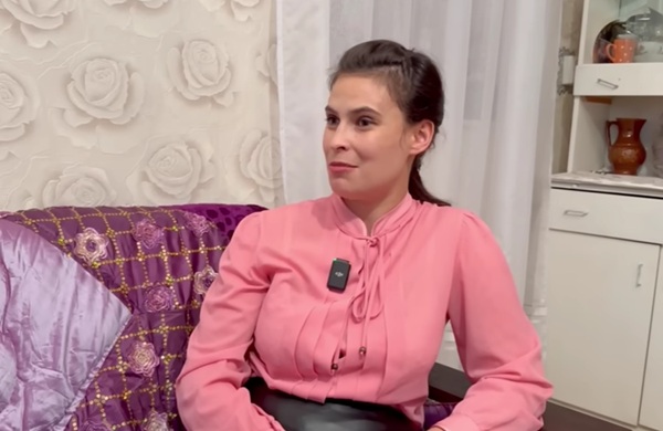 femeie bruneta cu parul prins imbracata in roz sta pe o canapea