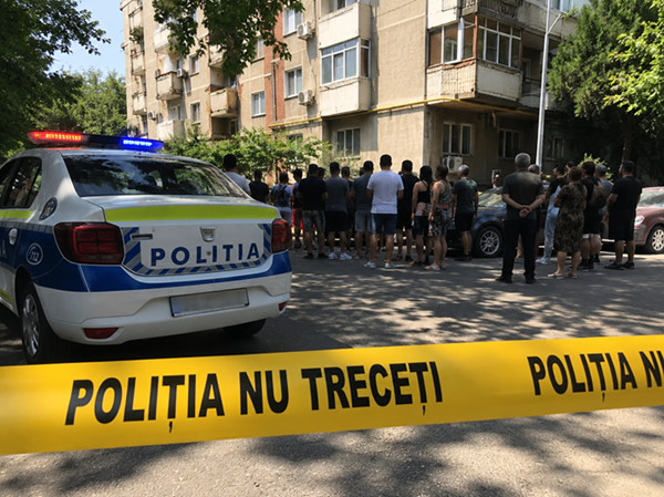 mai multe persoane stranse langa un bloc de locuinte si o masina de politie