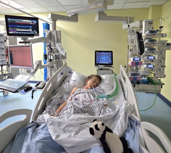 baiat blond sta pe un pat de spital conectat la aparate