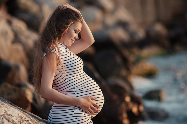femeie insarcinata imbracata in rochie alba cu dungi negre