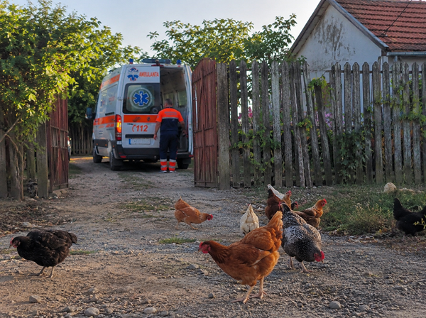 o ambulanta asteapta la o poarta in mediul rural intr o curte in care se plimba gaini