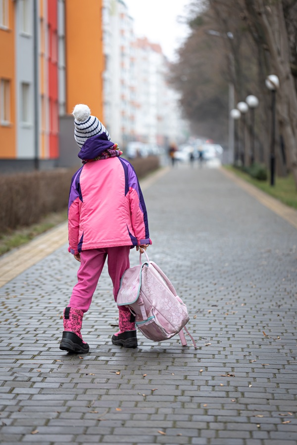 copil imbracat in roz merge pe strada cu ghiozdanul in mana