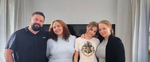 barbat si femeie alaturi de doua fete adolescente intr-o camera cu televizor